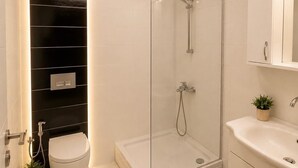 Un baño moderno con cabina de ducha de vidrio, inodoro y lavamanos con espejo.