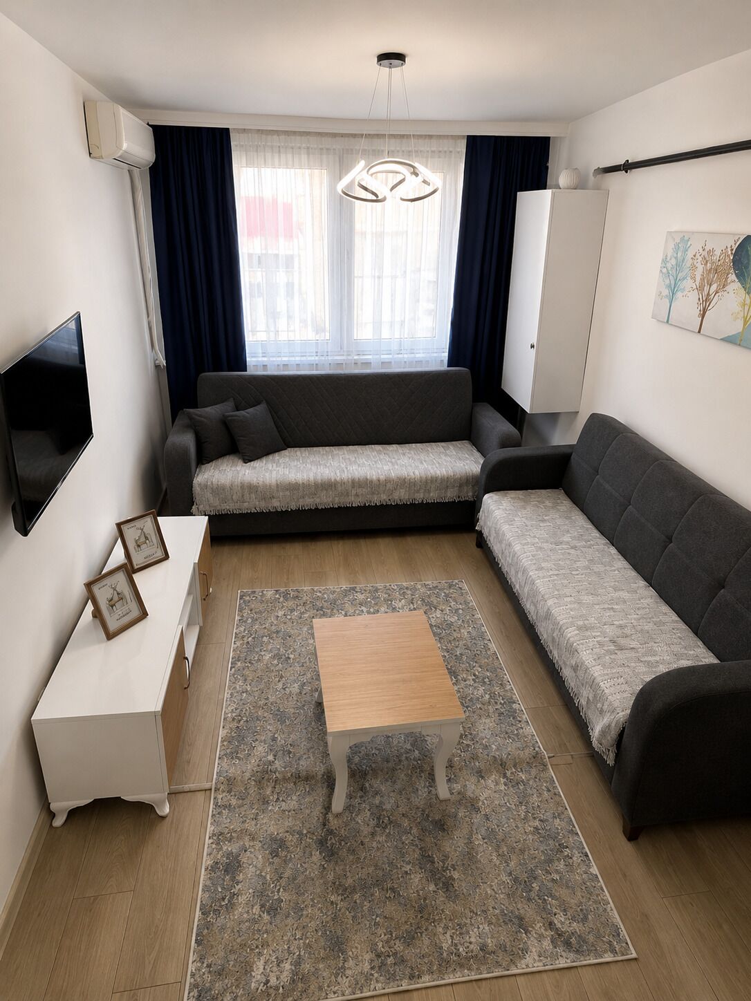 A modern living room with a sofa, a coffee table, a flat-screen TV, and a window with curtains.