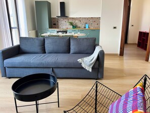 Ein modernes Wohnzimmer mit einem grauen Sofa, einem schwarzen runden Tisch und einem farbenfrohen Kissen.
