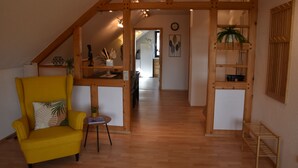 Een kamer met een geel fauteuil, houten balken, een whiteboard en een plant.