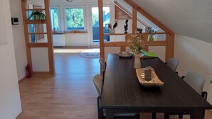 Een eetgedeelte met een houten tafel, stoelen, een vaas met bloemen en uitzicht op het exterieur door grote ramen.
