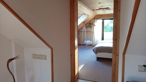 Een smalle gang die leidt naar een slaapkamer met een schuine kap, een houten schommelstoel en een bed.