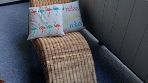 Een rieten loungeset met twee kussens op een balkon met uitzicht op huizen en bomen.