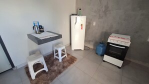 Une cuisine compacte équipée d’un réfrigérateur, d’une cuisinière à gaz, d’un petit plan de travail et de quelques tabourets.