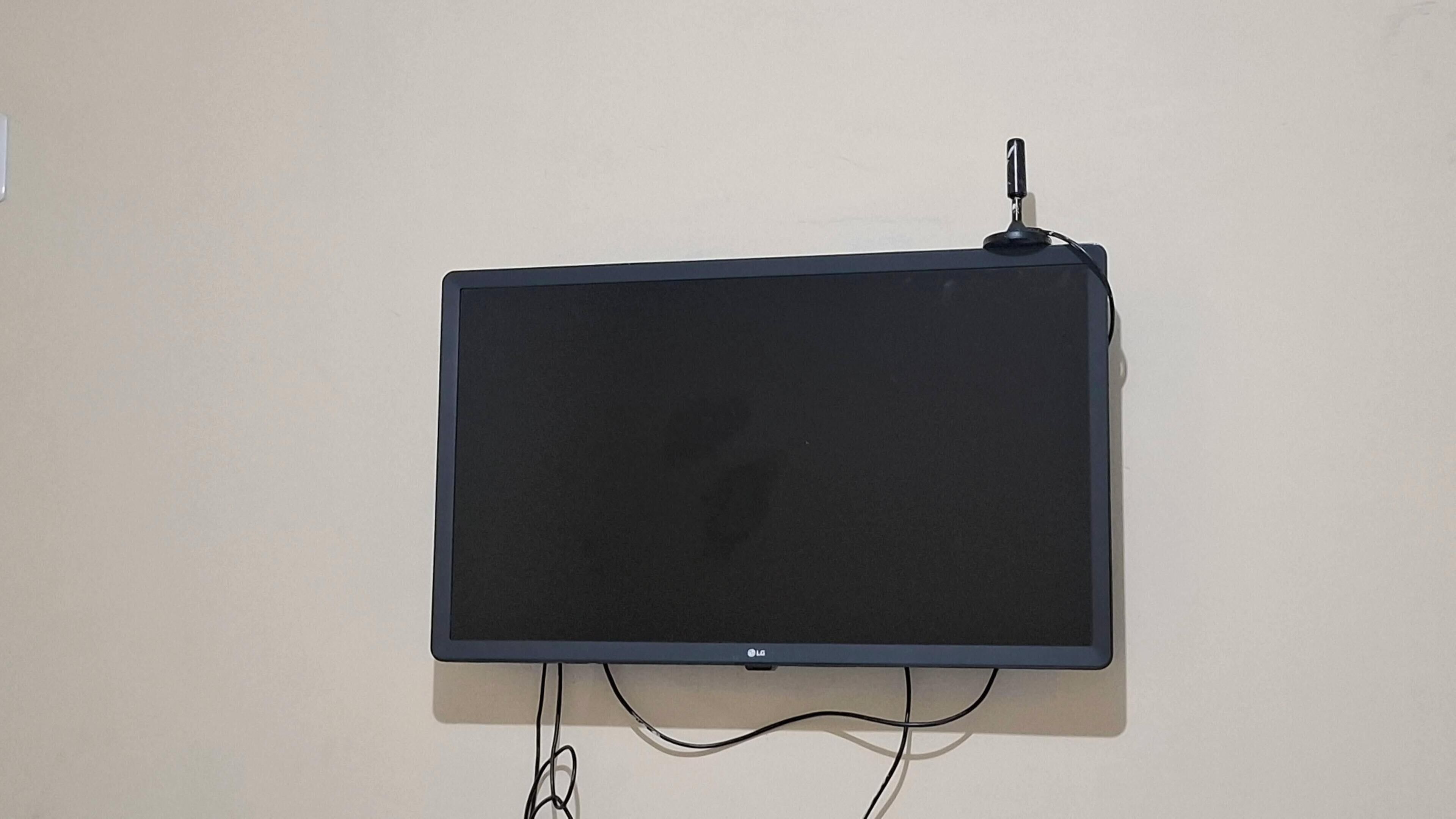 Televisão de tela plana presa na parede, com um cabo conectado.