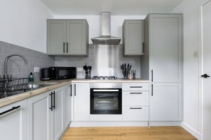 Een kleine keuken met witte kastjes, een roestvrijstalen afzuigkap, een magnetron en een oven.