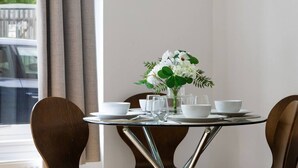 A dining table with white bowls, glasses, and a vase of white flowers, set against a window with curtains. - Forth Court City Retreat (Stirling)