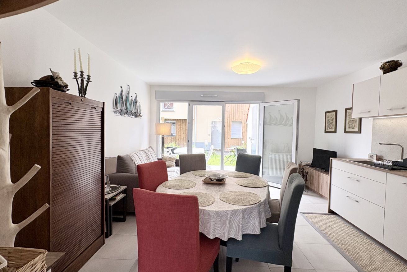 Un coin repas avec une table ronde, des chaises et une vue sur l’extérieur, visible à travers une porte vitrée.