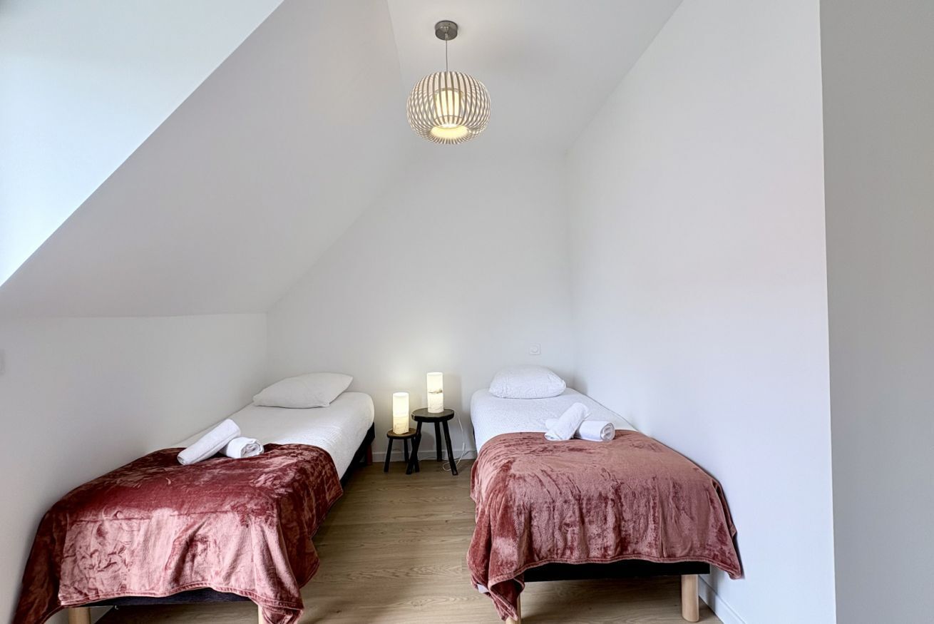 A room with two beds, each with a headboard and a pillow, and a small table between them.