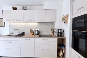 Et moderne køkken med hvide skabe, en træbordplade, en vask, kaffemaskine og ovn.