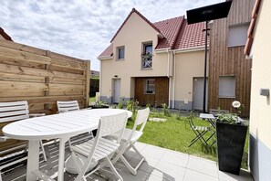 En boligejendom med terrasse, rundt bord og hvide stole.