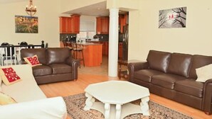 A living room with a brown leather sofa, a white coffee table, and a kitchen in the background. - The Peaceful Court House in Kitchener (Kitchener)