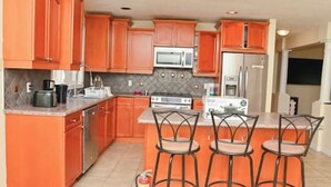 A kitchen with orange cabinets, a microwave, a stove, and three bar stools. - The Peaceful Court House in Kitchener (Kitchener)