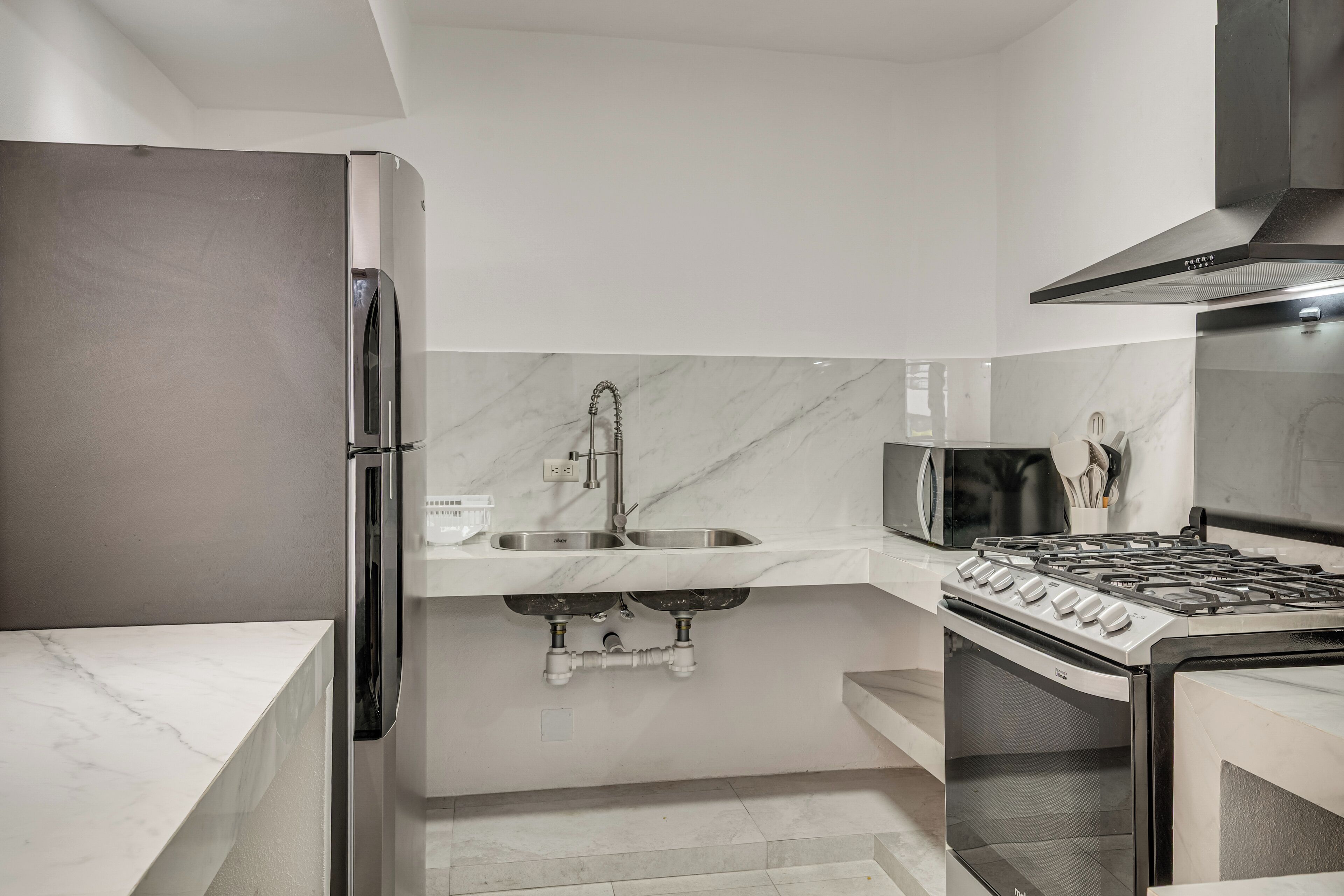 A modern kitchen with a stainless steel refrigerator, a built-in microwave, a gas stove, and a sink with a marble backsplash.