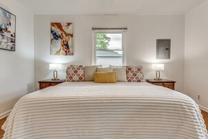 Quarto com cama grande, duas mesas de cabeceira, janela com persianas e um quadro de eletricidade na parede.