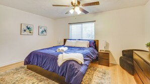 Ein Schlafzimmer mit Bett, Deckenventilator, Nachttisch, Schreibtisch und Fenster.