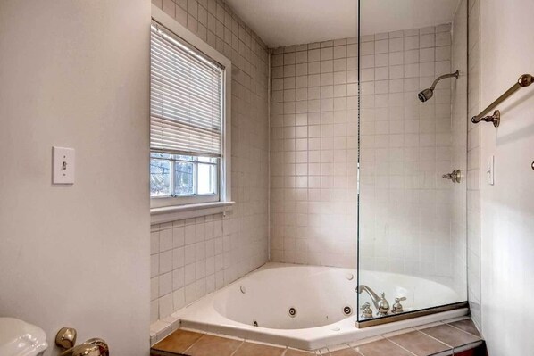 A bathroom with a glass-enclosed shower, a bathtub, and a window with blinds.