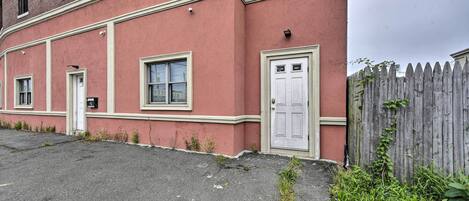 A red brick building with a white door and windows, a small garden area, and a wooden fence.