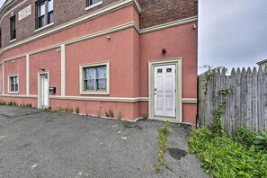 A red brick building with a white door and windows, a small garden area, and a wooden fence. - Pet-friendly Apartment, 6 Miles to Downtown (Revere)