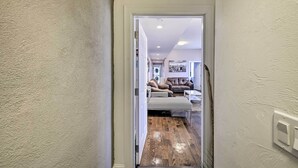 Un couloir qui mène à un salon aménagé avec un canapé, un pouf et un tapis.