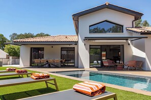 Ein modernes Haus mit Swimmingpool, Sitzgelegenheiten im Freien und einer Terrassenfläche.