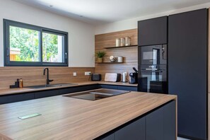 Eine moderne Küche mit einer großen Kochinsel, schwarzen Geräten, Holzböden und einem Fenster mit Blick auf Bäume.