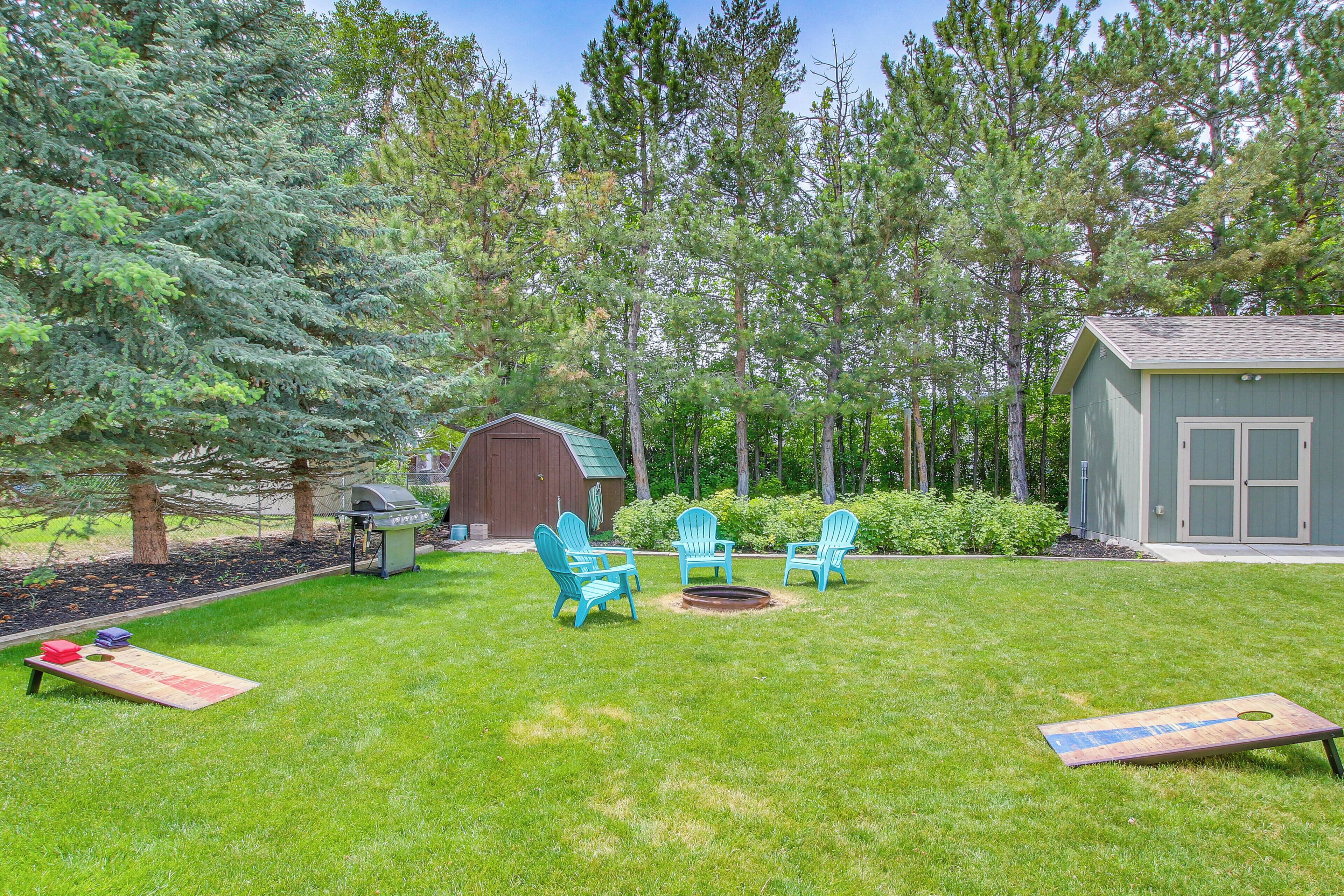 A backyard with a barbecue grill, a shed, and a play area with a fire pit and chairs.