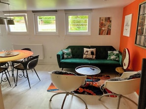 Un salon avec un canapé vert, une table de salle à manger ronde et un tapis coloré.