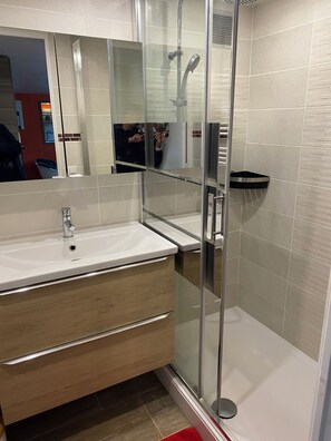A modern bathroom with a glass shower enclosure, a white sink, and a wooden vanity.