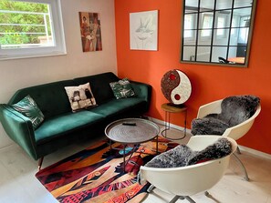 Un salon avec un canapé vert, un fauteuil blanc, une table basse ronde et un tapis coloré.