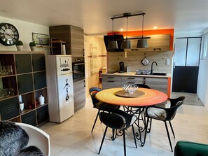 A modern kitchen with a dining area, featuring a refrigerator, oven, and a dining table with chairs.
