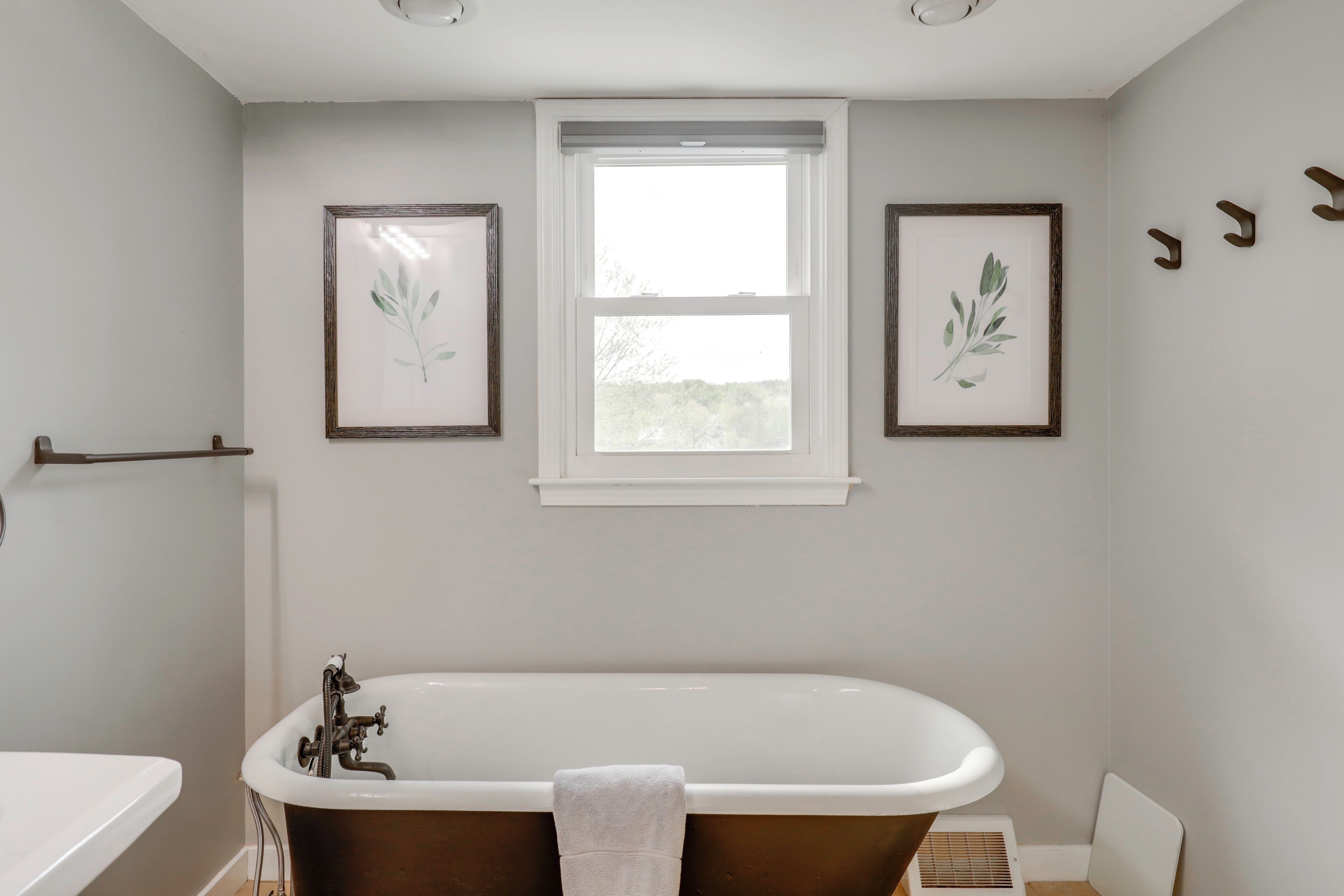 A bathroom with a bathtub, a window, and two framed botanical prints on the wall.
