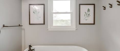 A bathroom with a bathtub, a window, and two framed botanical prints on the wall.