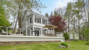 Ein zweistöckiges Haus mit Balkon, einer kleinen Gartenhütte und einem Rasen.