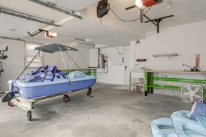 A boat on a trailer in a garage with a fan, a bicycle, and a table with a green surface. - Kayaks, Paddleboat! Lakefront Retreat in Barnstead (Center Barnstead)