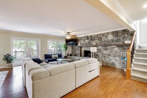 A living room with a sectional sofa, a fireplace, a staircase, and a view of the outdoors. - Dock & Lake Access! Family Escape in Osage Beach (Osage Beach)
