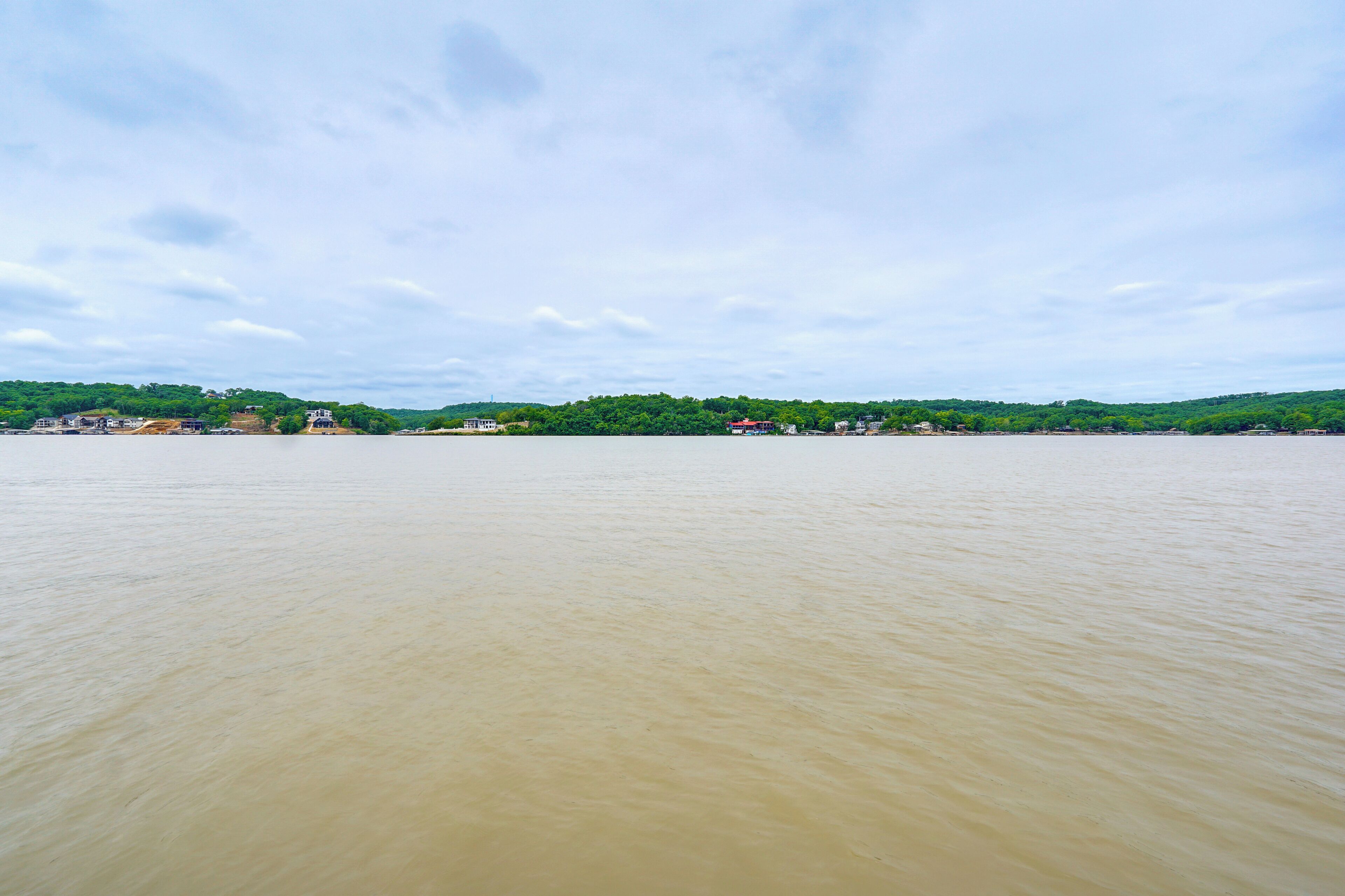 A river with a distant shoreline, buildings, and greenery.