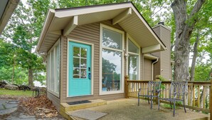 Un petit bâtiment en bois avec une porte bleue, un porche doté de bancs et un chemin de pierre menant à l’entrée.
