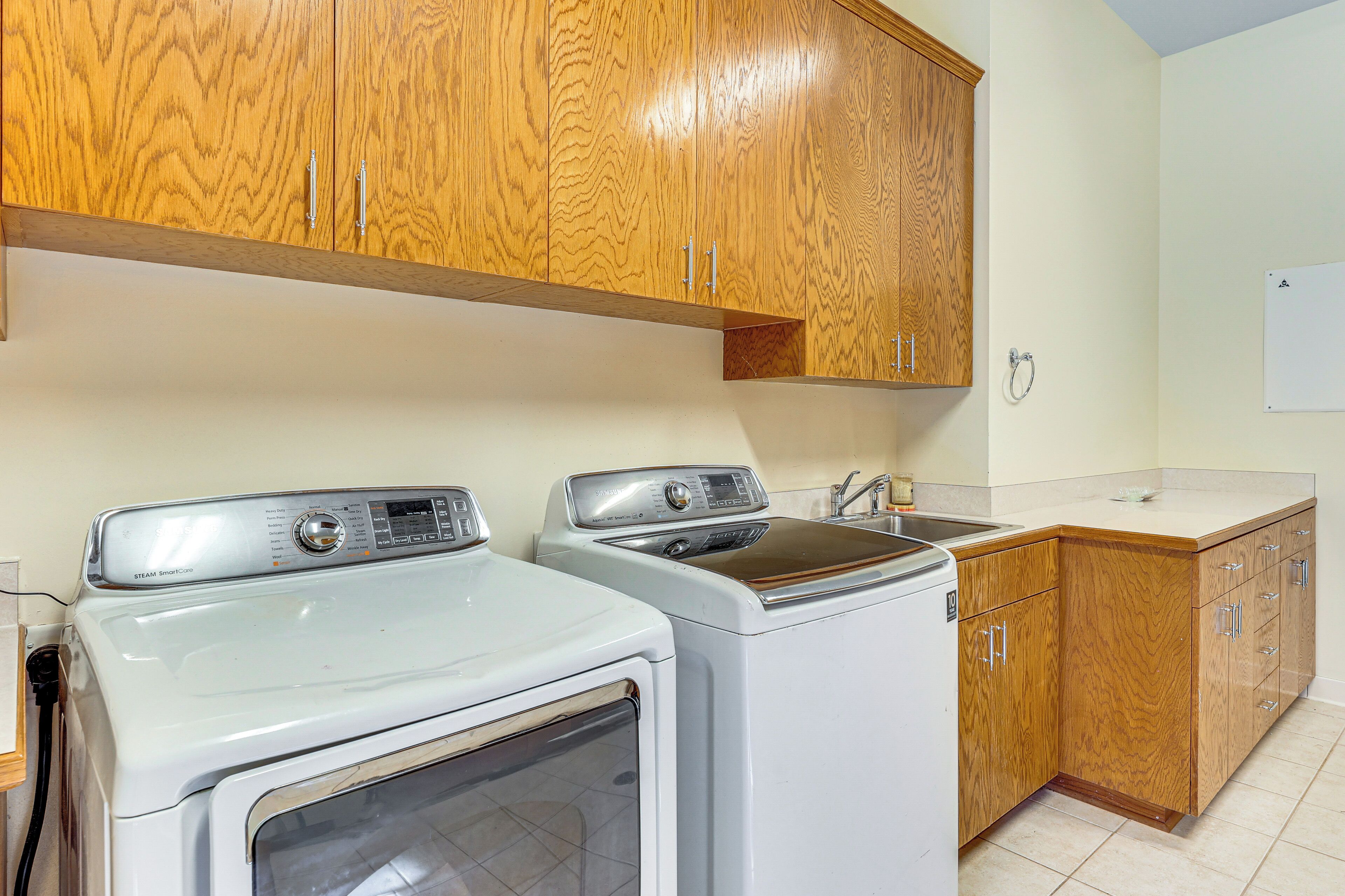 A laundry area with two washing machines, wooden cabinets, a sink, and a whiteboard on the wall.