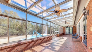 A covered patio with a brick floor, large windows, and a view of a swimming pool and trees. - Stocked Pond! 33-acre Lagrange Estate w/ 2 Units (LaGrange)