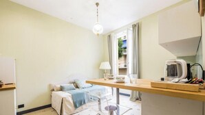 A small, well-lit room with a bed, a table with a lamp, a refrigerator, and a window with curtains. - The Riviera apartment, located on the ground floor of Villa Aranci in Via Fabio Filzi 2B, Genoa, offers an elegant and comfortable stay in an exclusive setting.With a private entrance, double bedroom, living area, private bathroom, and direct access to t (Genova)
