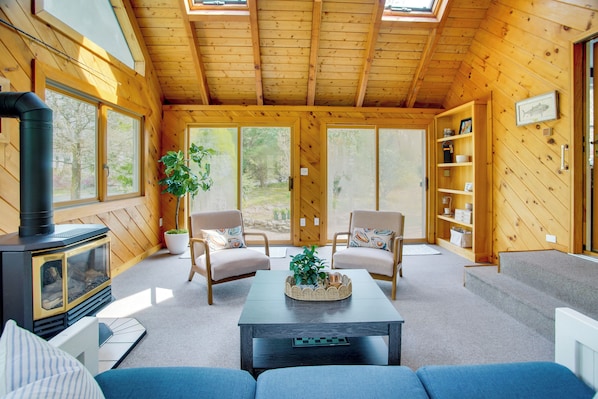 A cozy cabin interior with a fireplace, two armchairs, a coffee table, and a bookshelf. - 3 Mi to Nauset Beach! Family Home w/ Private Yard (Orleans)