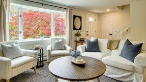 A living room with a sofa, armchair, and a coffee table. There is a window with a view of trees. - 3 Mi to Nauset Beach! Family Home w/ Private Yard (Orleans)