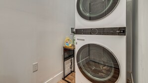 Une buanderie équipée de deux machines à laver superposées, d’une étagère sur laquelle se trouve une bouteille de lessive et d’une prise de courant.