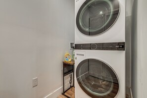 A laundry room with two stacked washing machines, a shelf with a bottle of detergent, and a power outlet. - 90-acre Gem w/ Custom Pool & 2 Ponds in Jefferson (Jefferson)