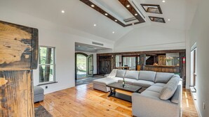 Un vaste espace de vie comprenant un grand canapé d’angle, un plancher en bois et un design moderne au niveau du plafond.