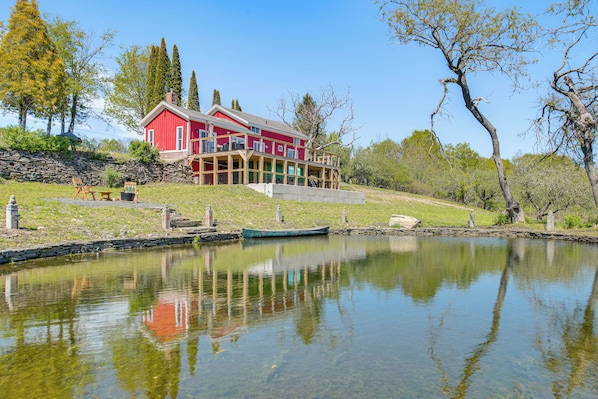 A red house with a balcony, a pond, and stone walls.