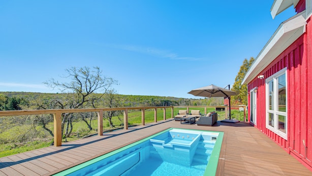 Une piscine sur une terrasse en bois, avec un bâtiment rouge en arrière-plan.