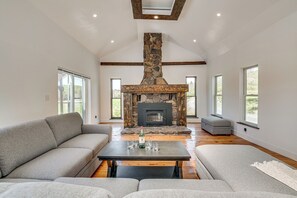 A spacious living room with a stone fireplace, a grey sectional sofa, and a coffee table with glasses and a bottle. - 90-acre Gem w/ Custom Pool & 2 Ponds in Jefferson (Jefferson)