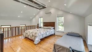 Une chambre avec un grand lit, un lit plus petit, un plancher en bois, un balcon et un plafond en pente doté d’un éclairage encastré.
